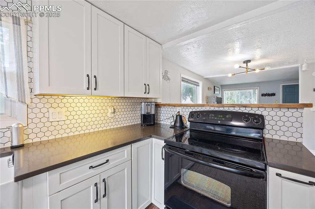 Image 7 of 36: Kitchen featuring decorative backsplash, dark countertops, white cabinetry,