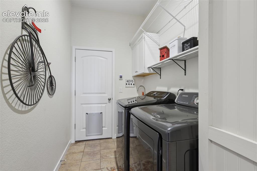 Image 19 of 50: Laundry space featuring tile flooring, white cabinetry, integrated shelving