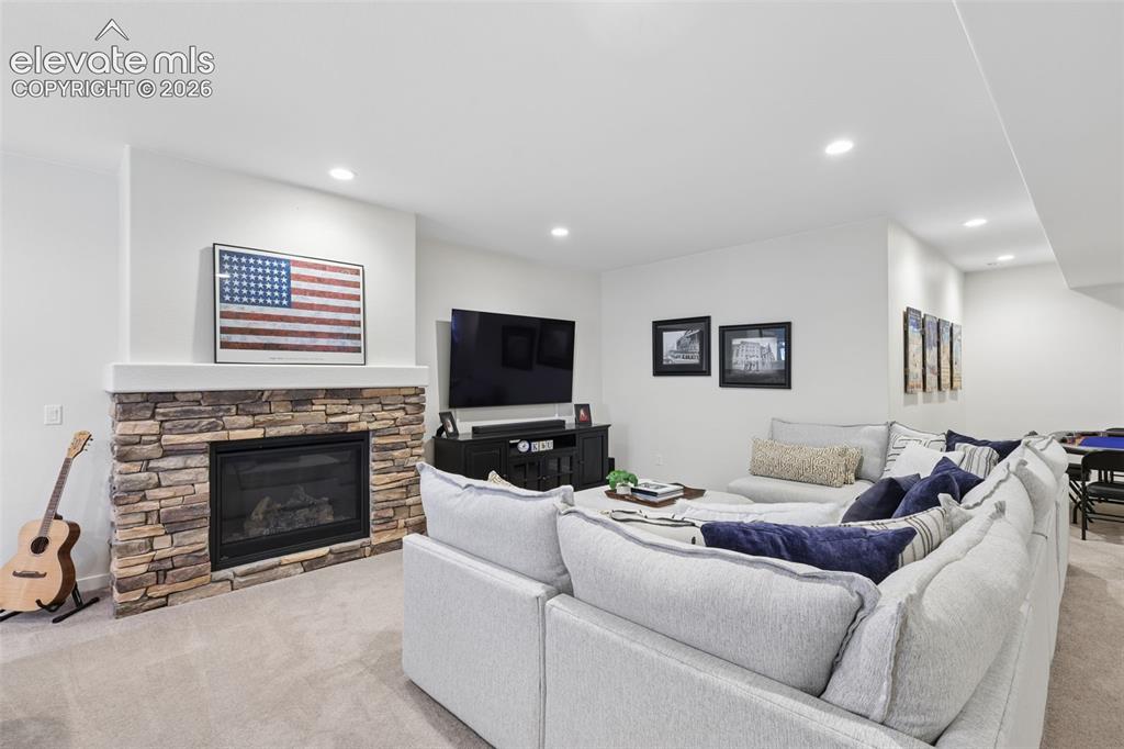 Image 32 of 50: Finished basement recreation room featuring a stone-surround fireplace with