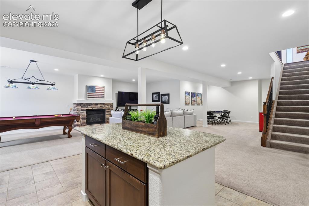 Image 34 of 50: Open-concept lower level with recessed lighting, a stone-faced fireplace, a
