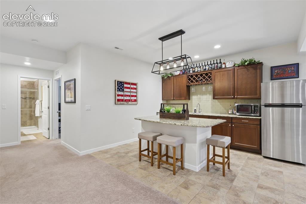 Image 35 of 50: Built-in wet bar with wood cabinetry, granite-style countertop, and tile fl