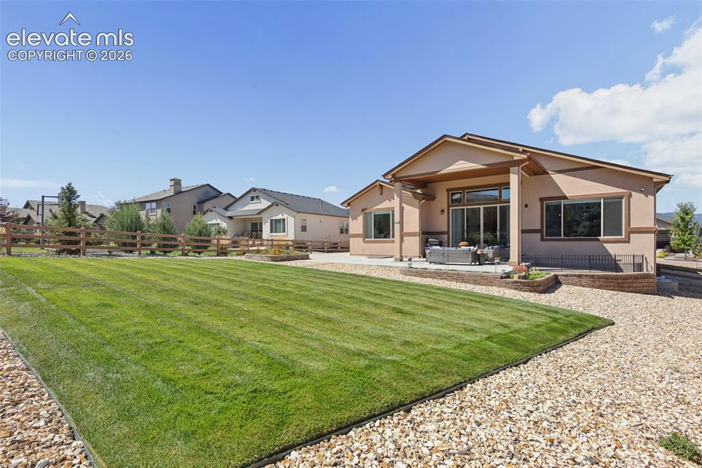 Image 47 of 50: Expansive lawn area with gravel border, wood fence, and stucco exterior