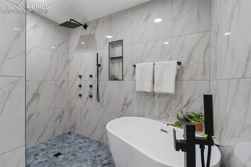 Image 21 of 48: Bathroom with a soaking tub, a tile shower, and tile walls