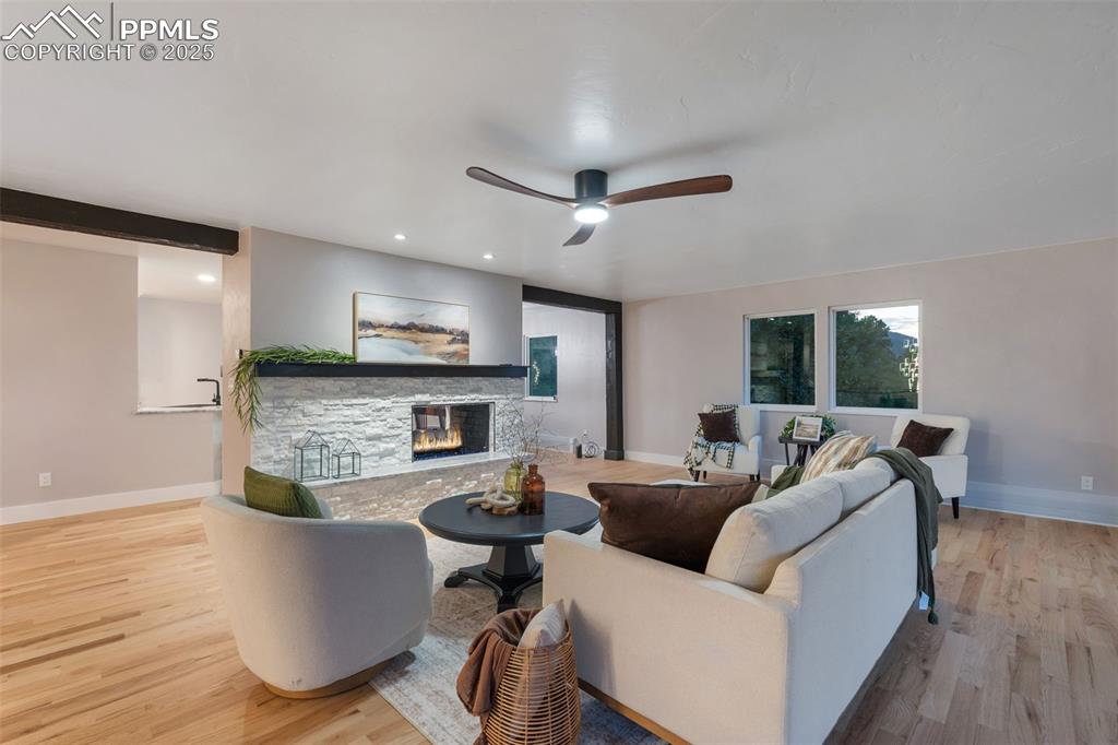 Image 5 of 48: Living room featuring a ceiling fan, wood finished floors, a stone fireplac