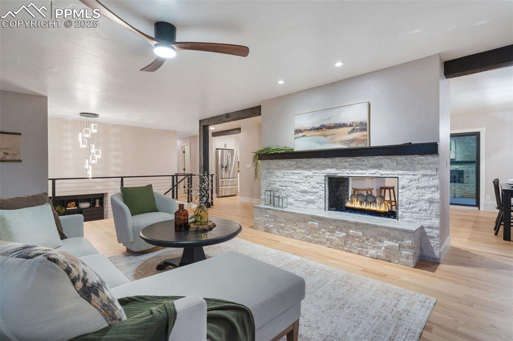 Image 6 of 48: Living area featuring a stone fireplace, wood finished floors, ceiling fan,
