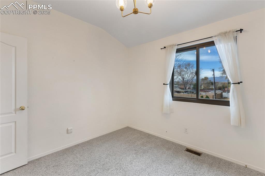 Image 19 of 37: Unfurnished room with lofted ceiling, a chandelier, and carpet flooring