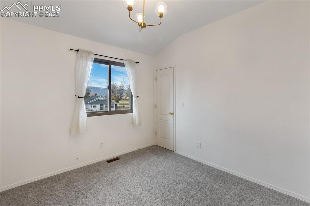 Image 20 of 37: Spare room with carpet, vaulted ceiling, and a chandelier