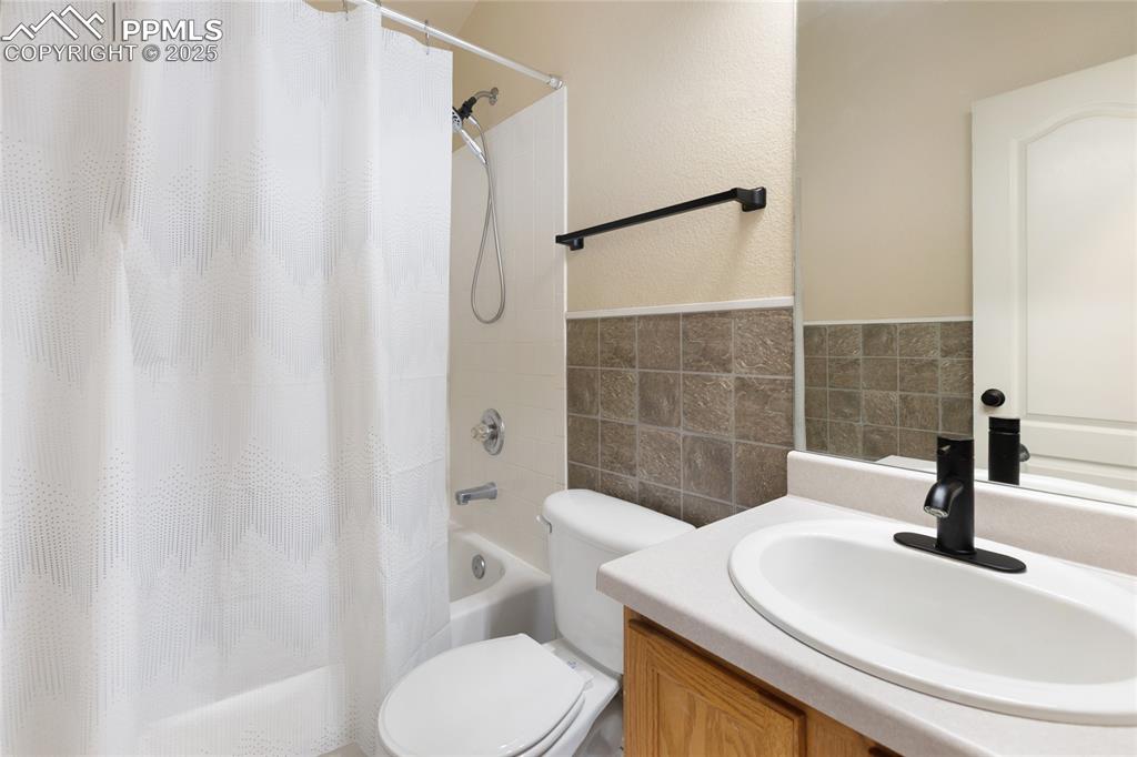 Image 23 of 37: Full bathroom with vanity, tile walls, shower / tub combo with curtain, a t
