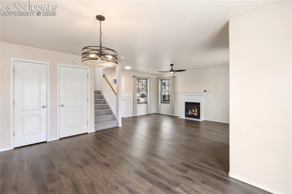 Image 7 of 37: Unfurnished living room with a chandelier, dark wood-style flooring, stairw
