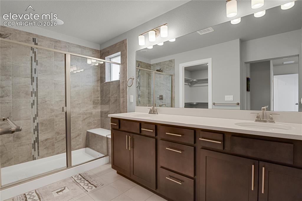 Image 12 of 28: En-suite bath with dual sinks, quartz counter, and oversized tiled shower