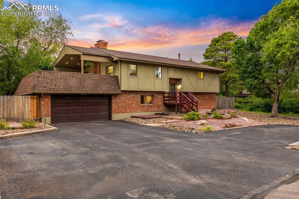 Caption: Split foyer home with driveway, brick siding, a chimney, and roof with shingles