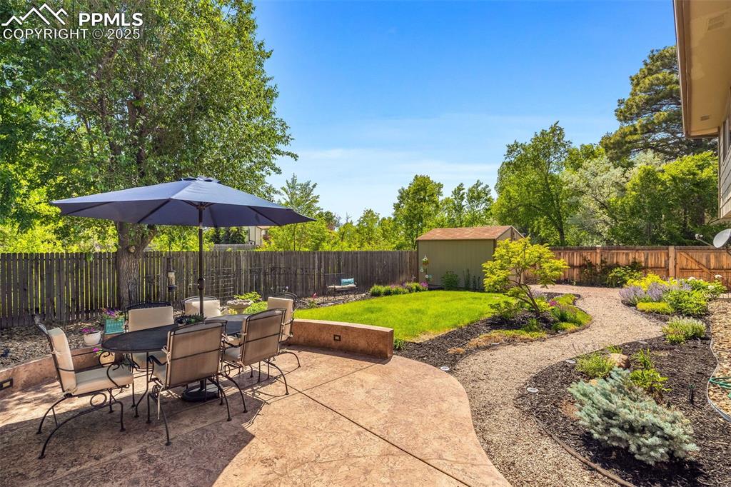 Image 32 of 47: Fenced backyard with a patio area, outdoor dining space, and a storage unit