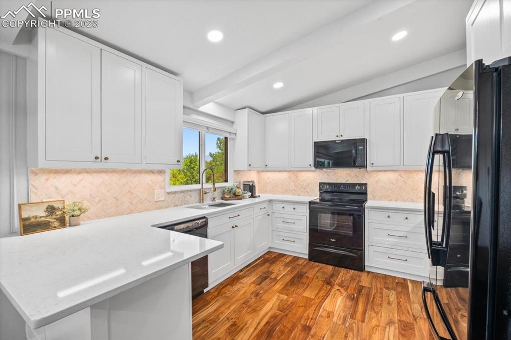 Image 4 of 47: Kitchen with black appliances, a peninsula, decorative backsplash, dark woo