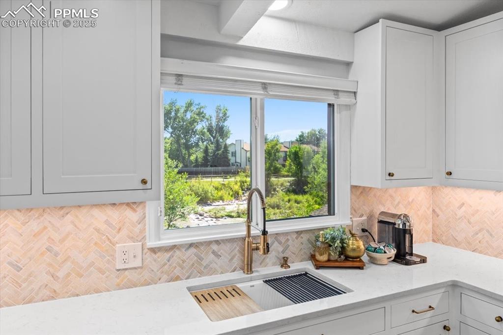 Image 7 of 47: Kitchen with light stone counters, tasteful backsplash, and white cabinetry