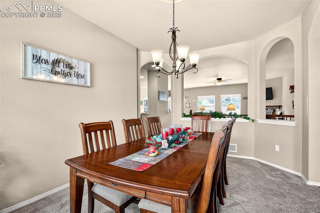 Image 7 of 48: Dining space with arched walkways, carpet flooring, a ceiling fan, a chande