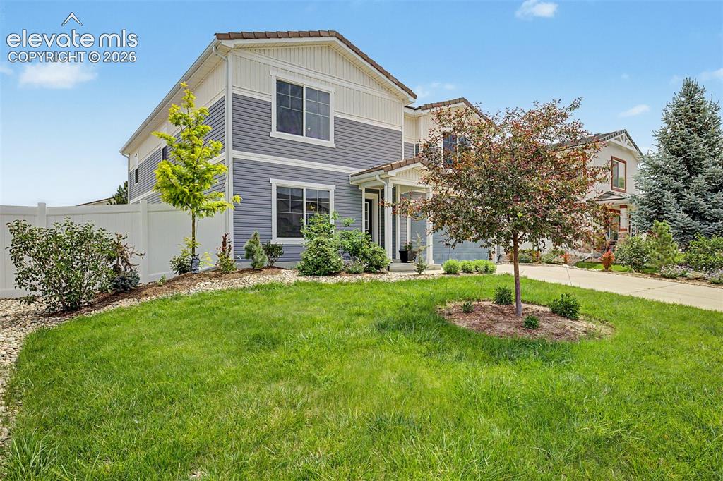 Image 2 of 43: Mature ornamental trees and lush garden beds frame the side of the home, sh