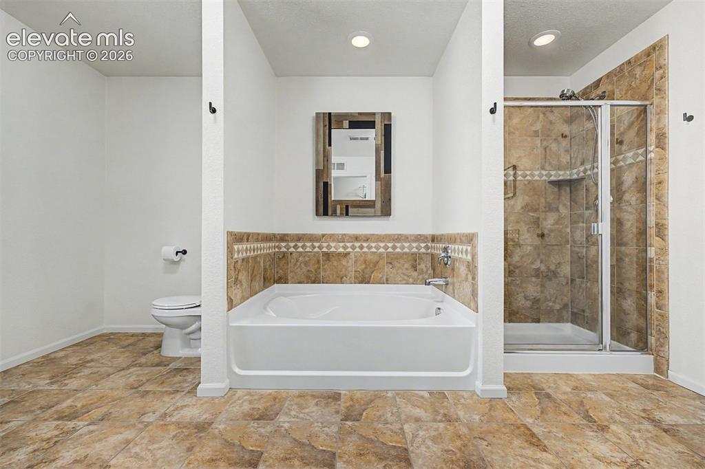 Image 26 of 43: A deep soaking tub framed in warm stone tile sits beside a glass-enclosed s