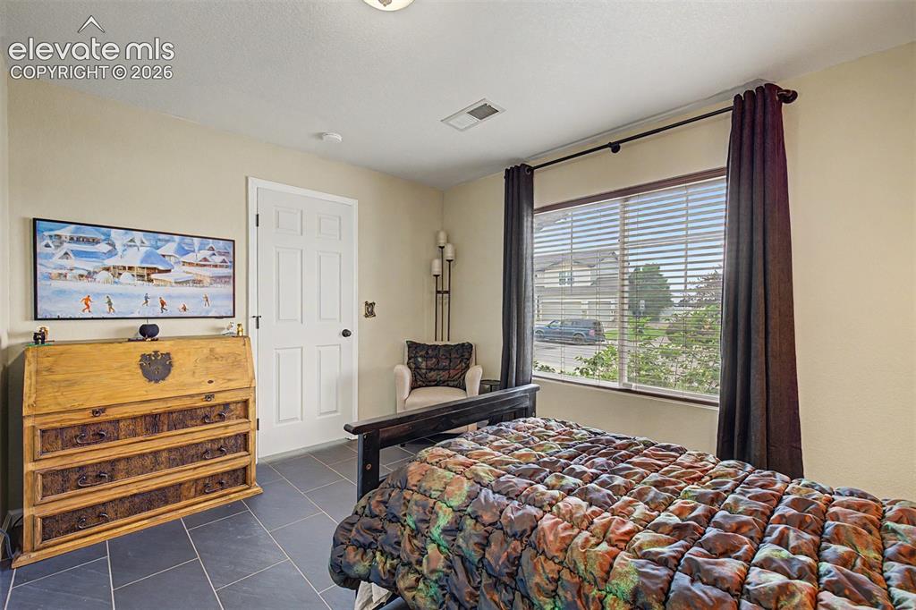 Image 28 of 43: Warm tones, dark tile flooring, and a large window give this bedroom a cozy
