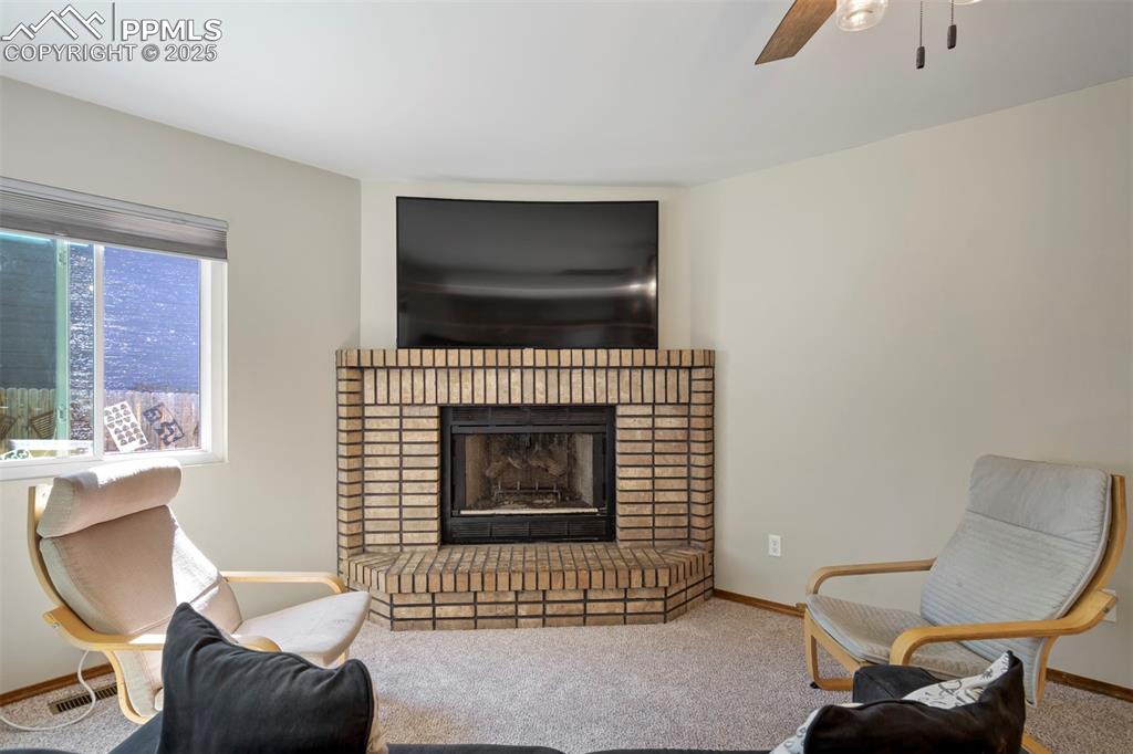 Image 11 of 50: Living room with a brick fireplace, carpet, and a ceiling fan