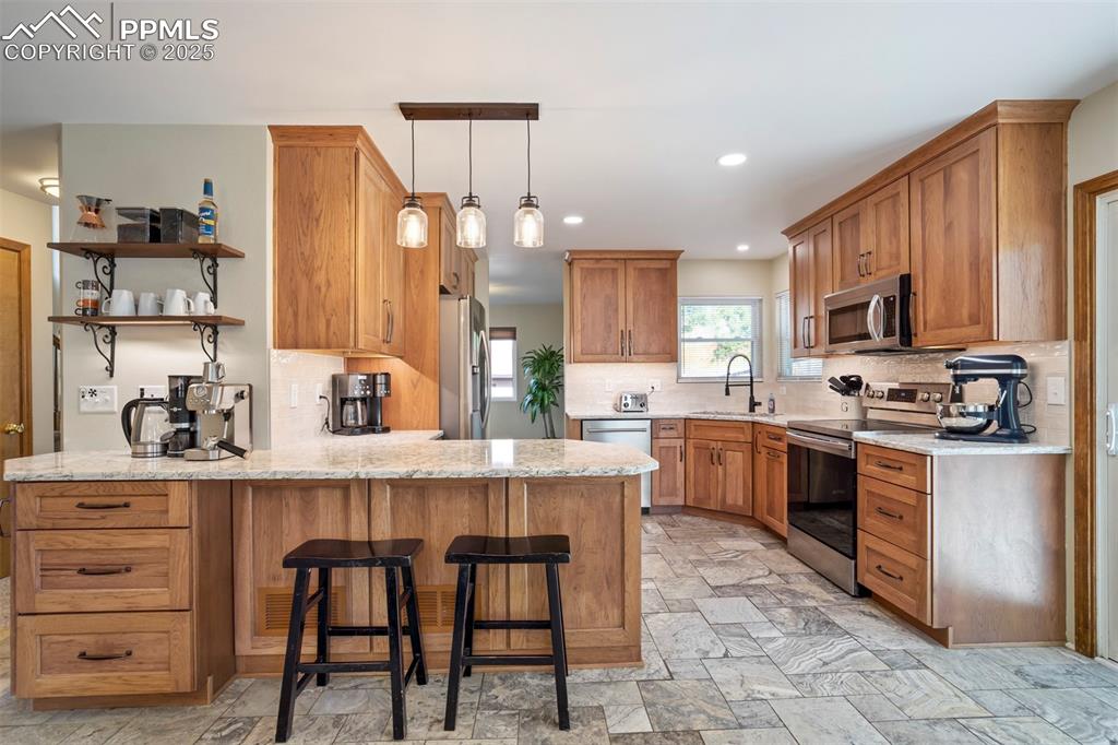 Image 15 of 50: Kitchen featuring a peninsula, stainless steel appliances, backsplash, ligh
