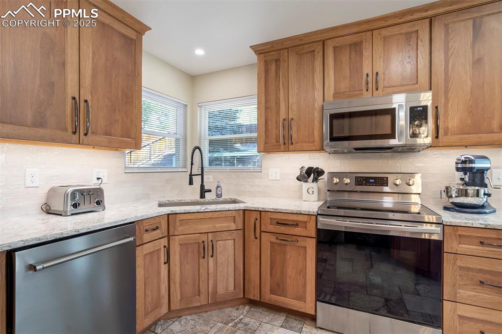 Image 19 of 50: Kitchen featuring stainless steel appliances, brown cabinets, decorative ba
