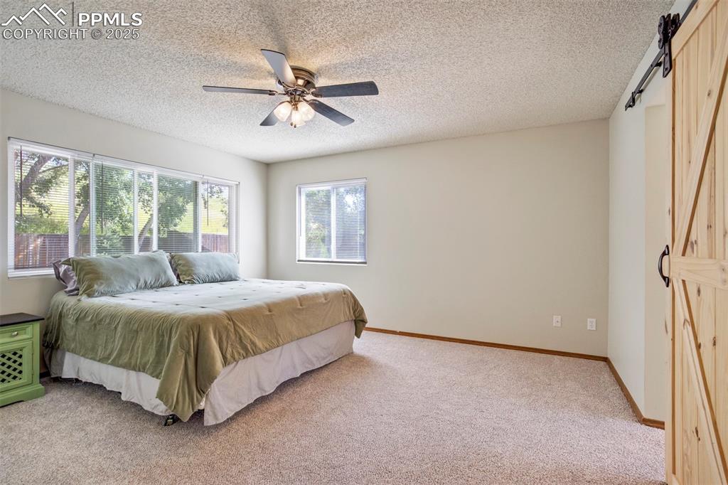 Image 21 of 50: Bedroom with light colored carpet, a barn door, a textured ceiling, and a c