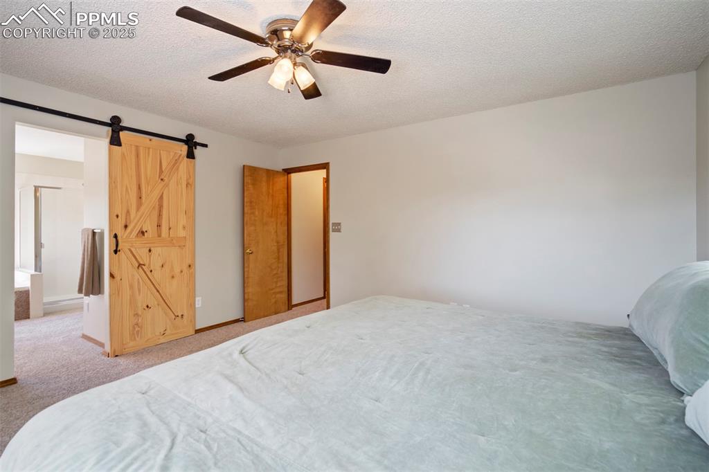 Image 23 of 50: Carpeted bedroom with a barn door, a textured ceiling, and a ceiling fan