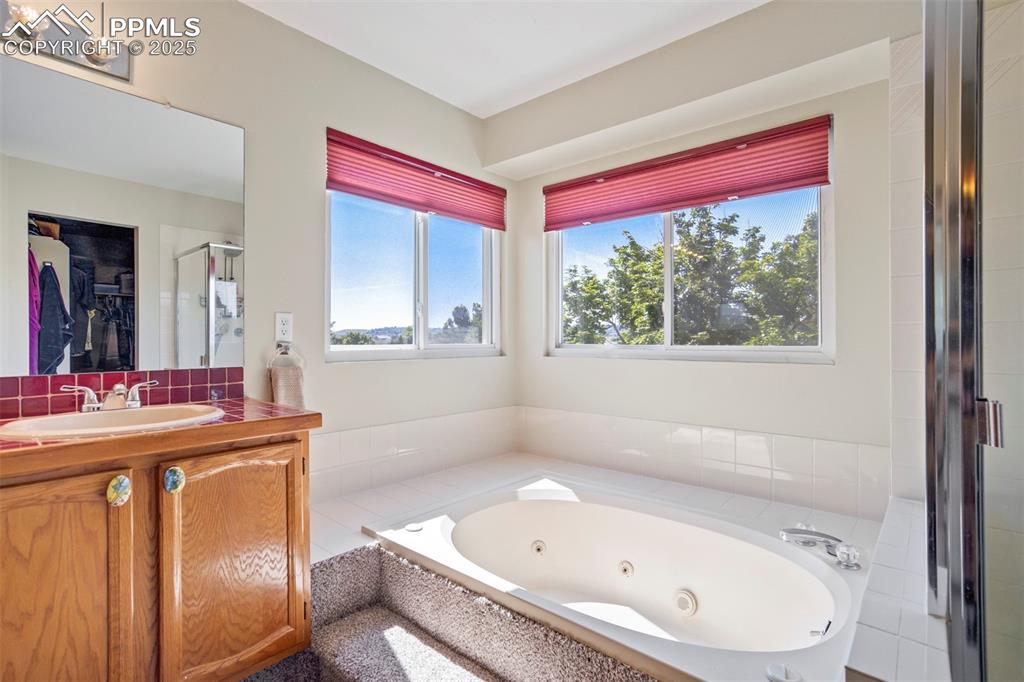 Image 27 of 50: Full bathroom with a tub with jets, a stall shower, and vanity