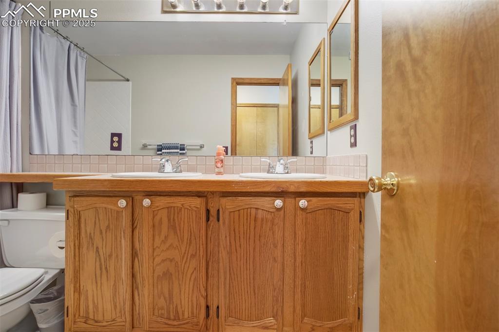 Image 33 of 50: Bathroom featuring double vanity, decorative backsplash, and a shower with