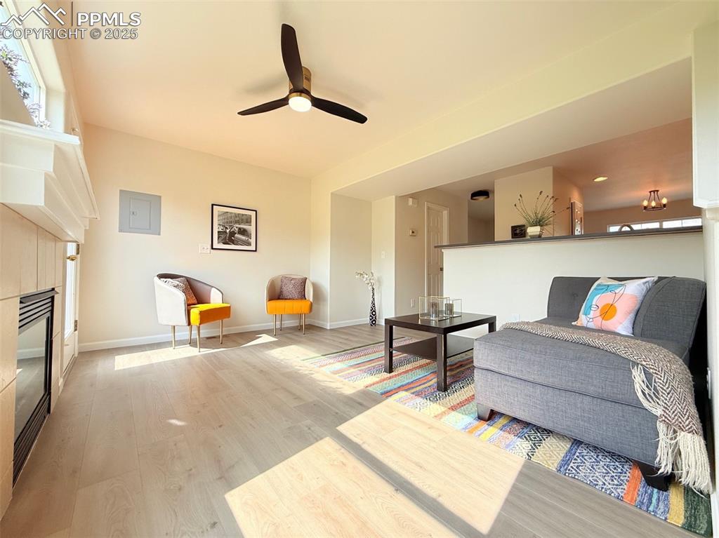 Image 9 of 44: Living area with light wood finished floors, a fireplace, a ceiling fan, an