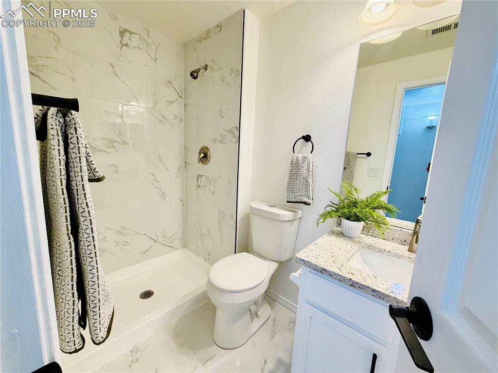 Image 23 of 38: Bathroom featuring vanity, a marble finish shower, and marble look tile flo