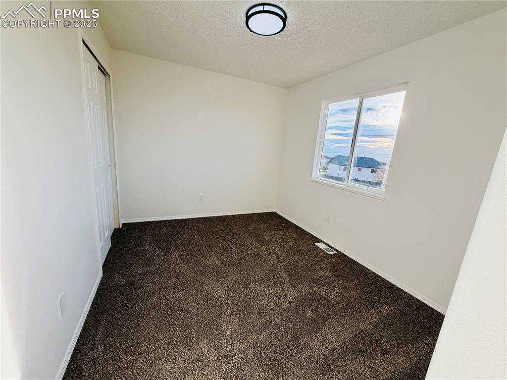Image 29 of 38: Unfurnished room with dark carpet and a textured ceiling