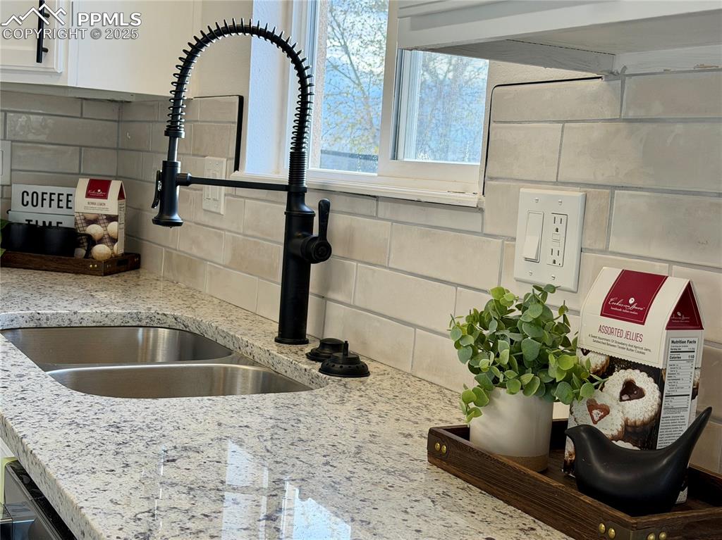 Image 9 of 38: Kitchen view of backsplash, light stone counters, and white cabinets