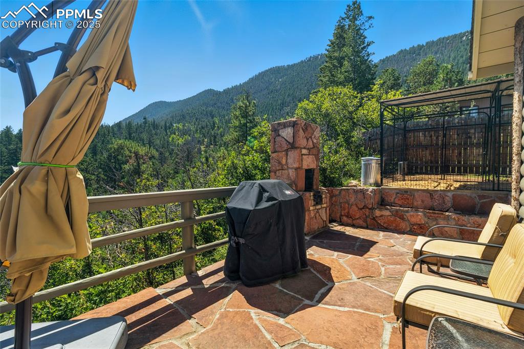 Image 12 of 43: View of patio featuring a wooded view, an outdoor stone fireplace, a mounta