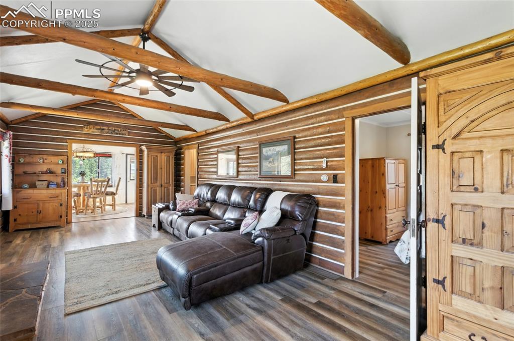 Image 17 of 43: Living area featuring beamed ceiling, rustic walls, dark wood-style floorin