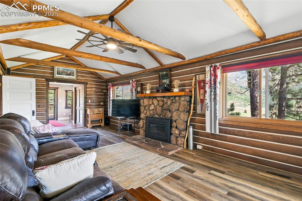 Image 19 of 43: Living room with beam ceiling, log walls, a stone fireplace, wood finished