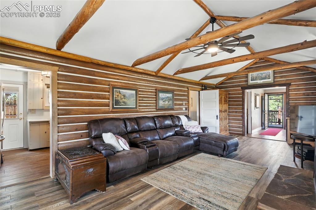 Image 20 of 43: Living area with rustic walls, beam ceiling, high vaulted ceiling, wood fin