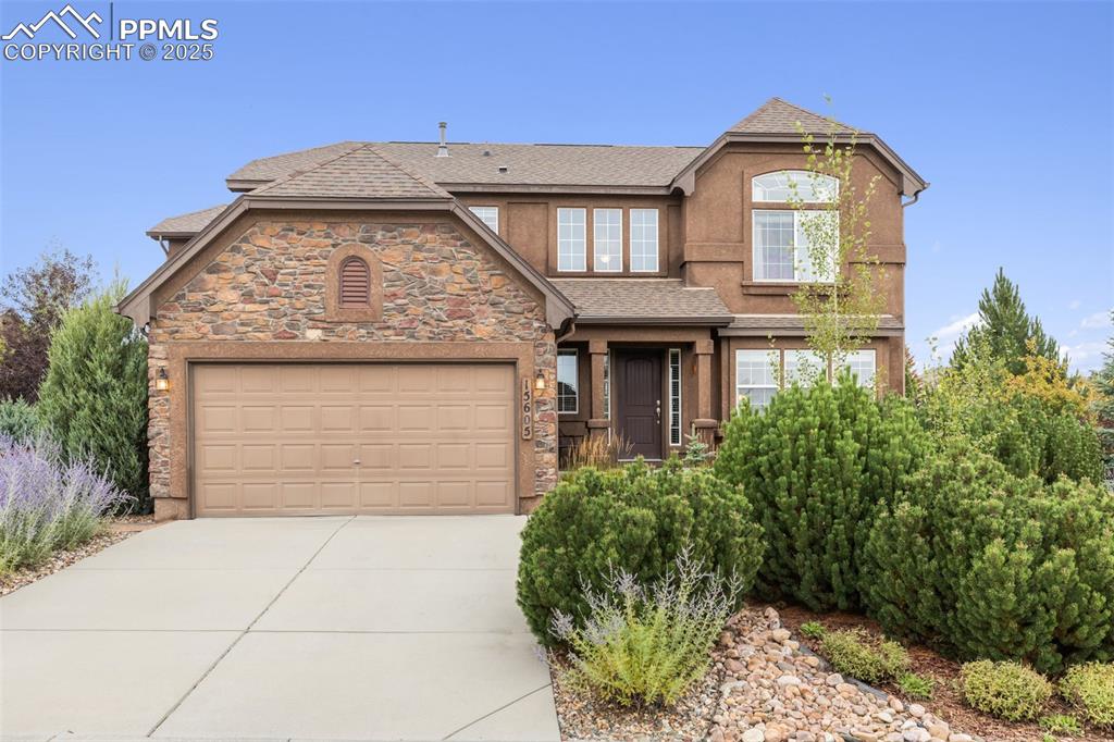 Caption: View of front of home with roof with shingles, concrete driveway, stone siding, and an attached gara