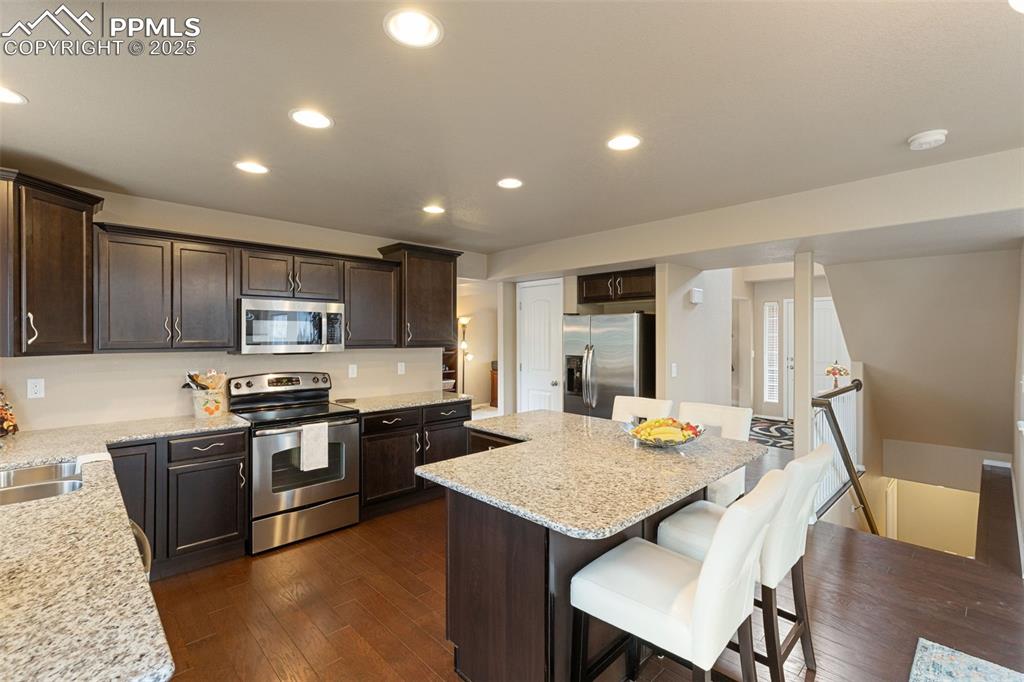 Image 13 of 50: Kitchen featuring dark brown cabinetry, appliances with stainless steel fin