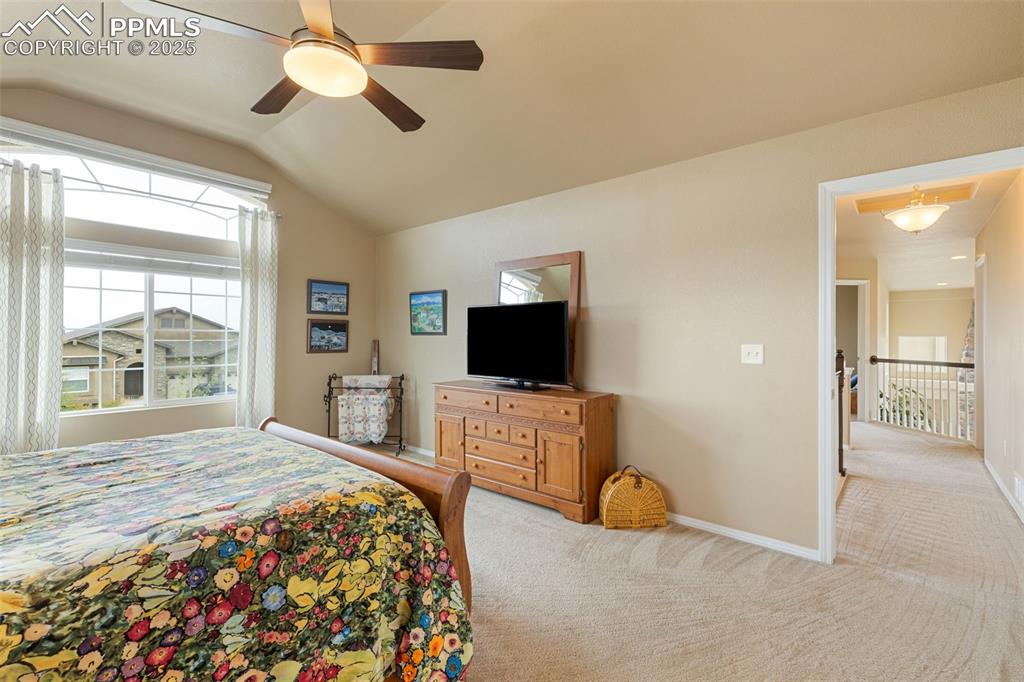 Image 23 of 50: Bedroom with light colored carpet, vaulted ceiling, and a ceiling fan