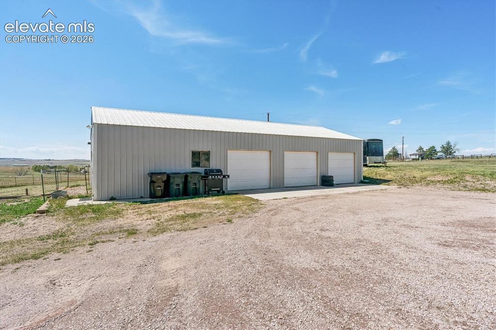 Image 23 of 34: Metal-sided outbuilding featuring three garage doors, a concrete pad, and a