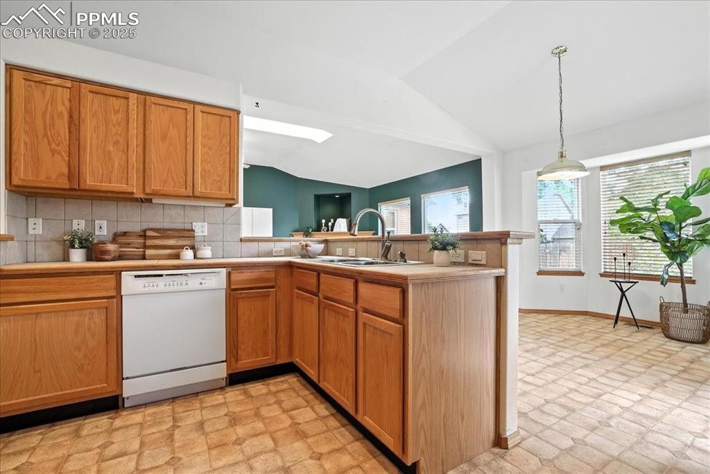 Image 11 of 50: Kitchen with vaulted ceiling, white dishwasher, backsplash, a peninsula, an