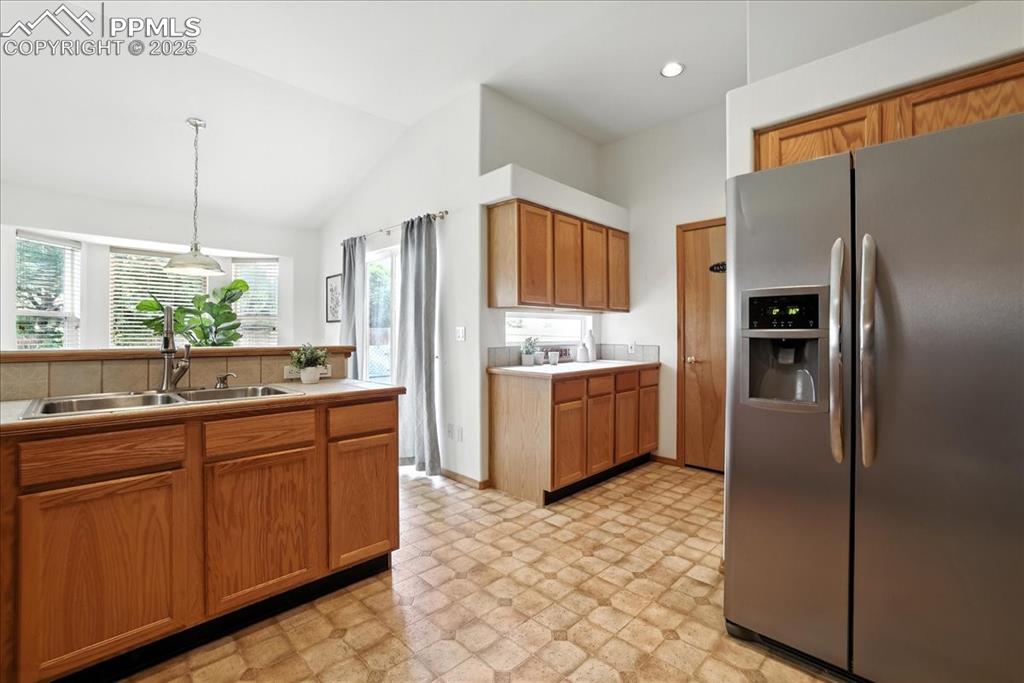 Image 12 of 50: Kitchen featuring stainless steel fridge, vaulted ceiling, light floors, li