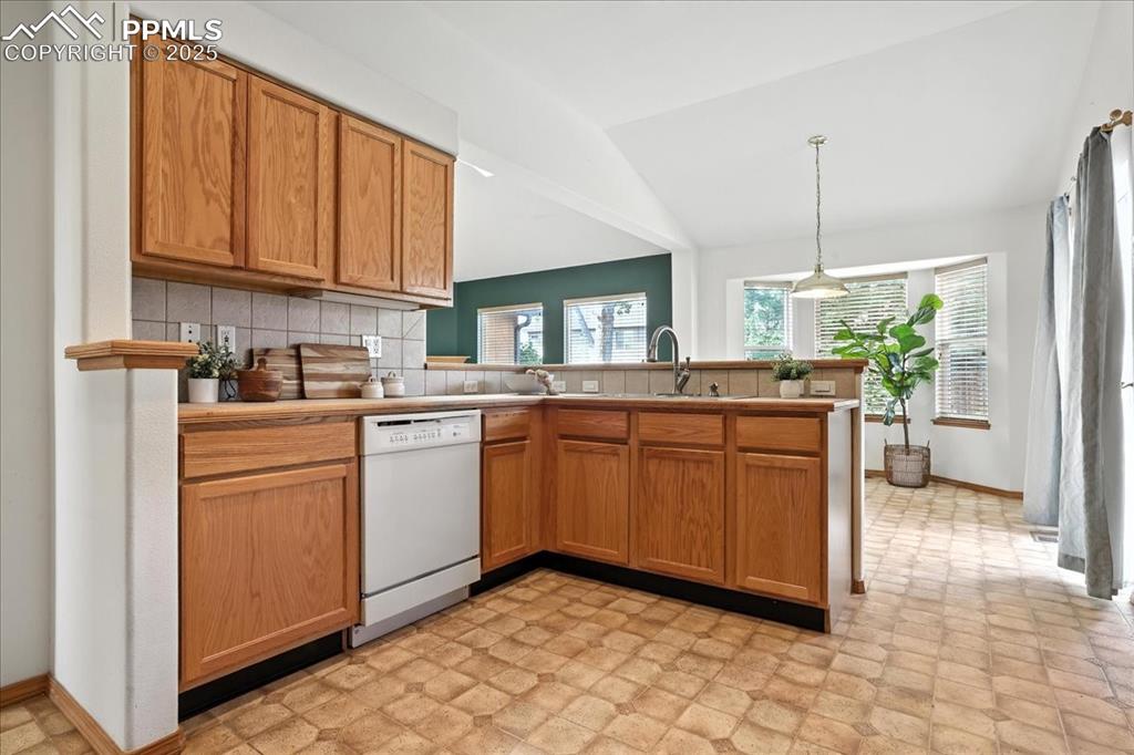 Image 13 of 50: Kitchen with backsplash, light flooring, vaulted ceiling, and white dishwas