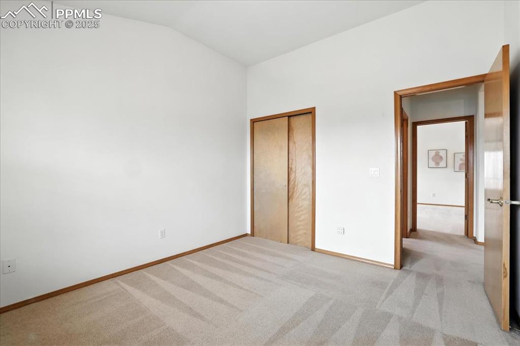 Image 22 of 50: Unfurnished bedroom with light colored carpet, vaulted ceiling, and a close