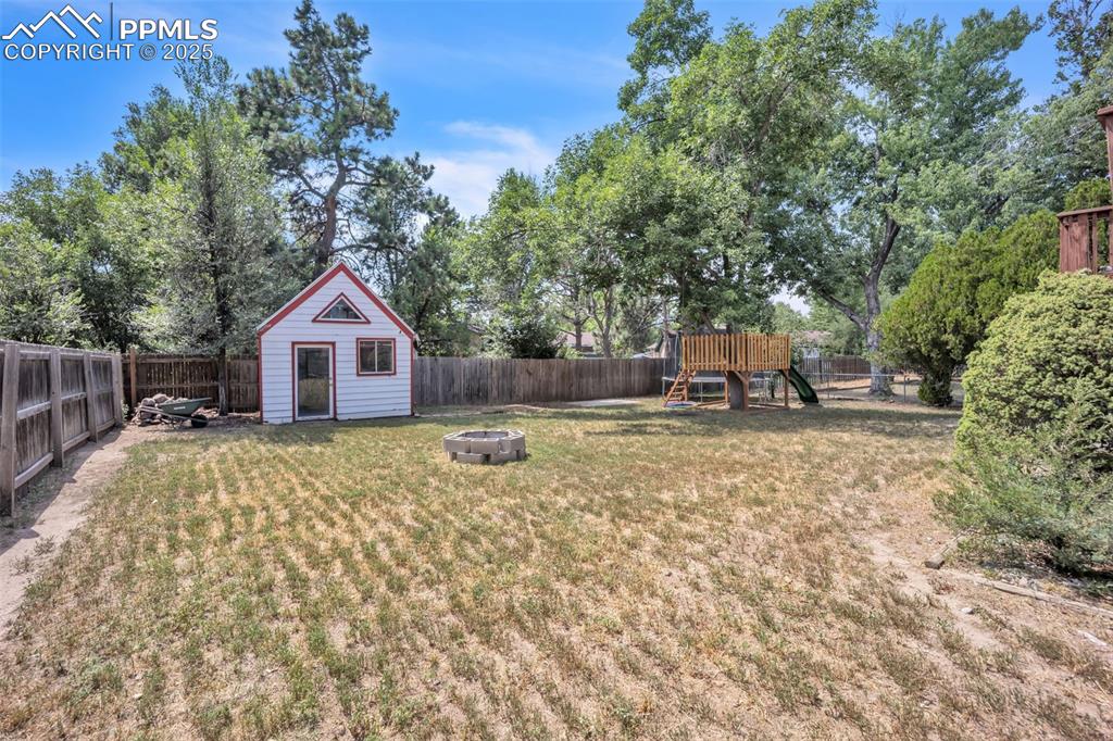 Image 34 of 34: Fenced backyard featuring a playground, a fire pit, and an outbuilding