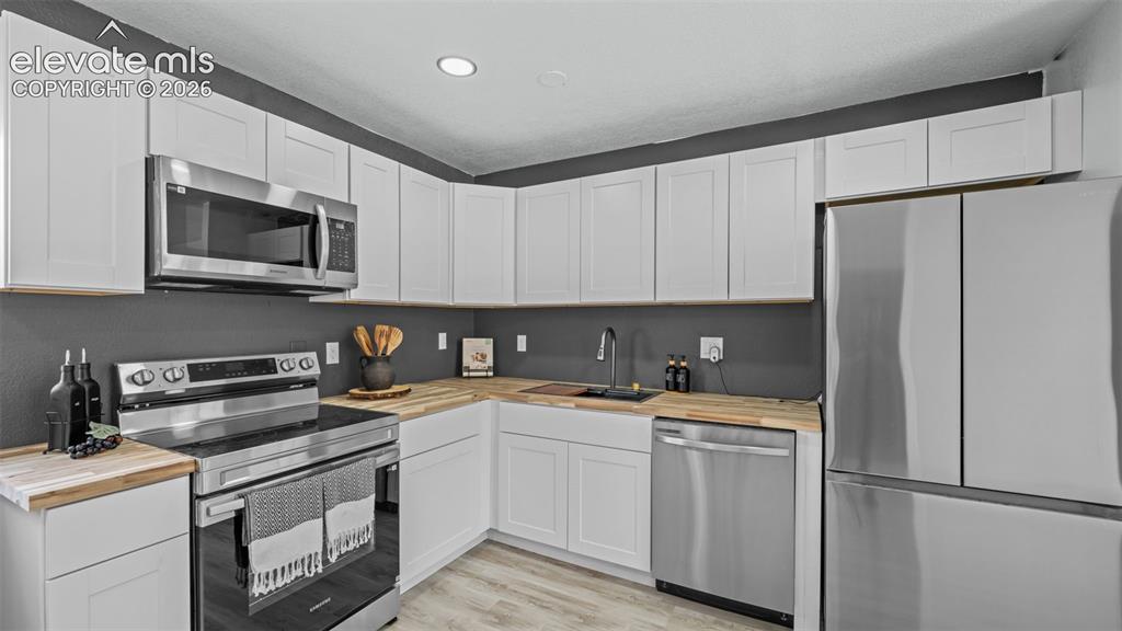 Image 11 of 31: White shaker-style cabinetry, wood-finish countertops, stainless steel appl