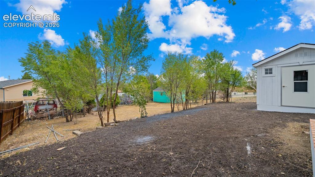 Image 19 of 31: Expansive rear yard with a newly cultivated ground, mature trees, and a woo