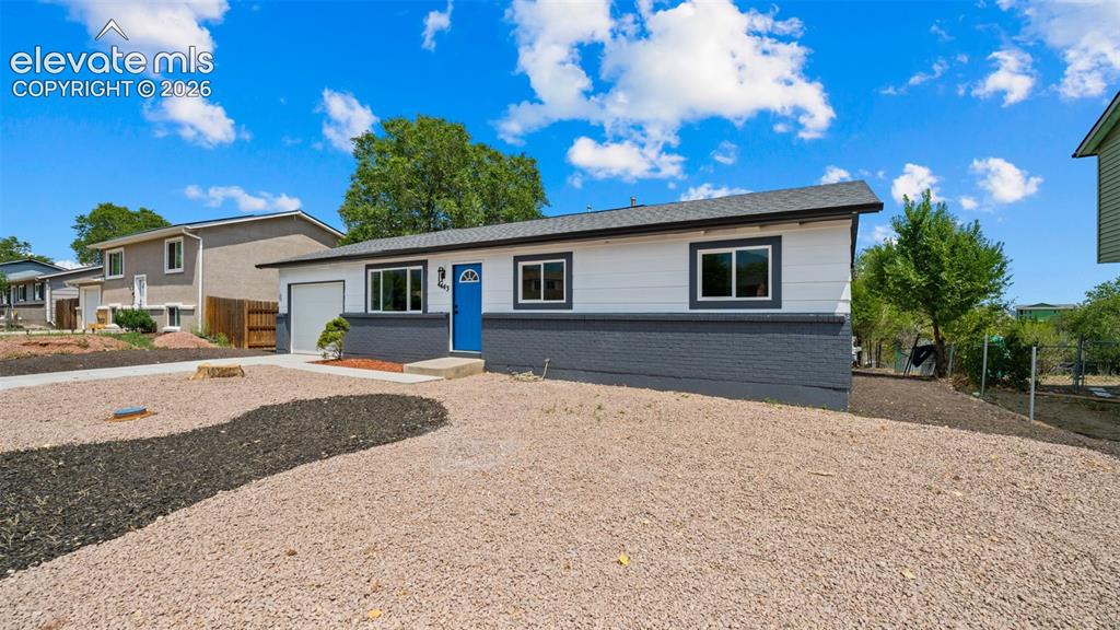 Image 2 of 31: Split-level exterior with a blue entry door, attached garage, and gravel la