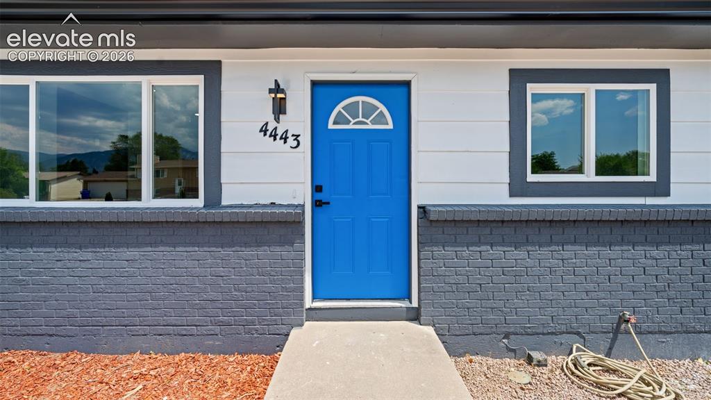 Image 4 of 31: White siding exterior with a blue entry door, dark brick foundation, and da